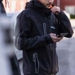 Kille i svart jacka håller mobiltelefon i handen